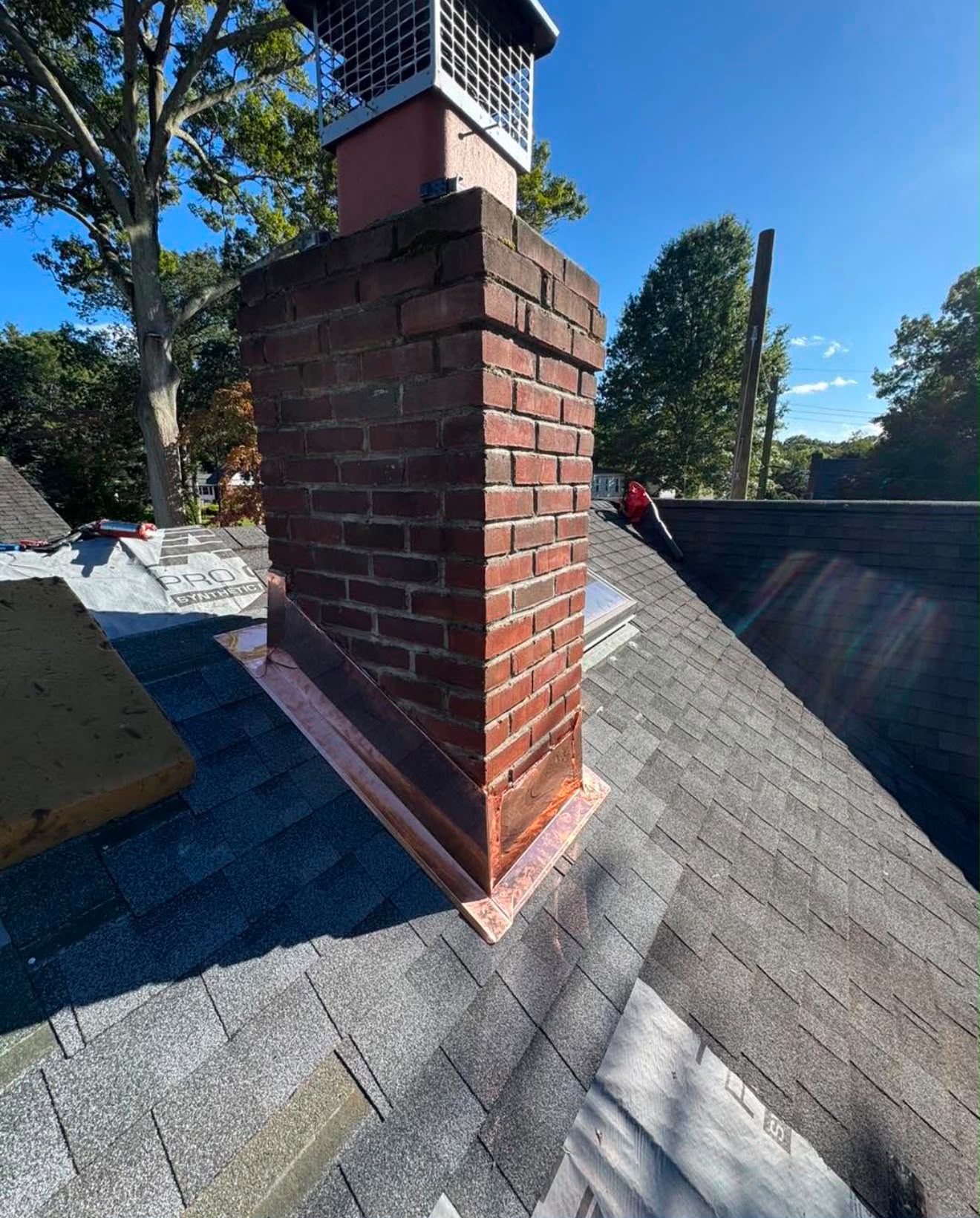New copper flashing installed around a brick chimney on a shingled roof
