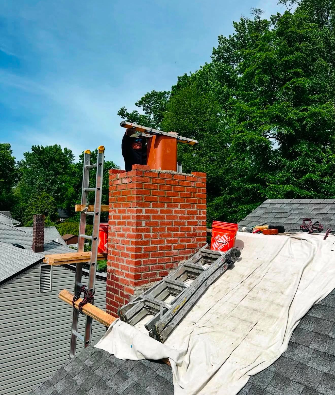 Technician lowering a clay flue liner into a brick chimney