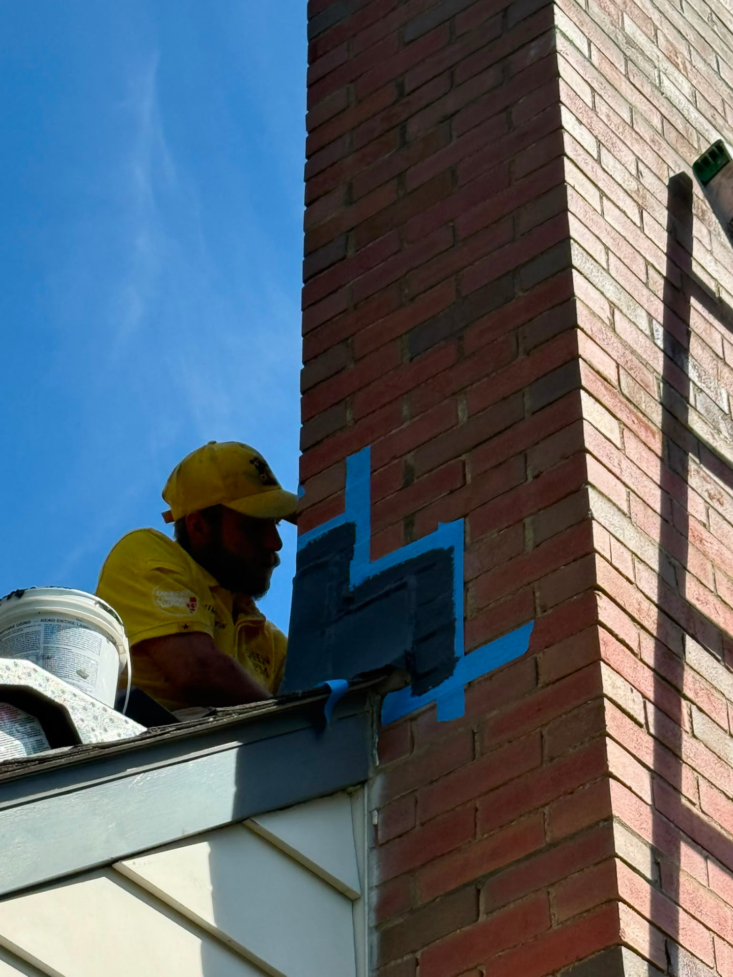 Technician applying sealant to a masked-off section of brick chimney