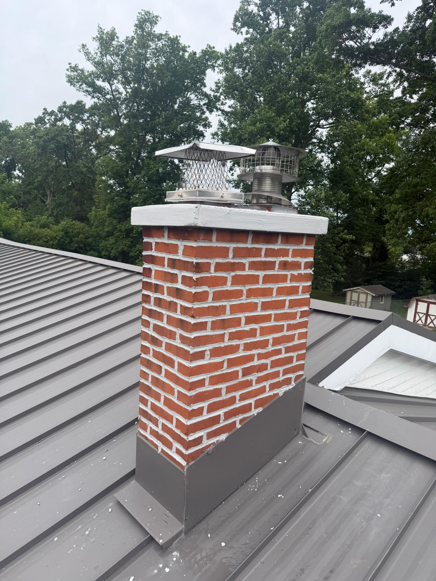 Two stainless chimney caps and a fresh white crown on a metal roof chimney