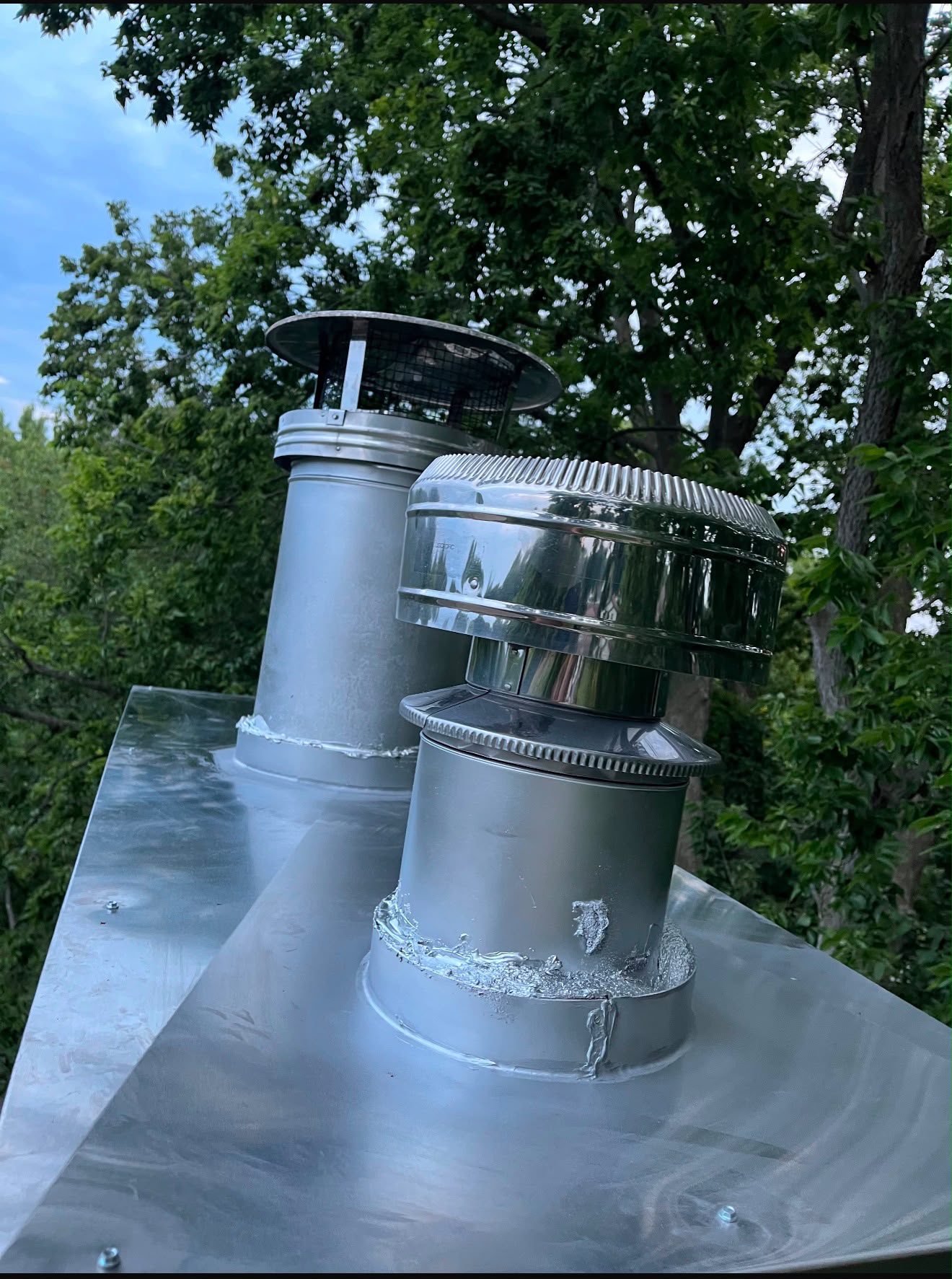 New stainless steel chimney caps and flashing pan installed on a chimney