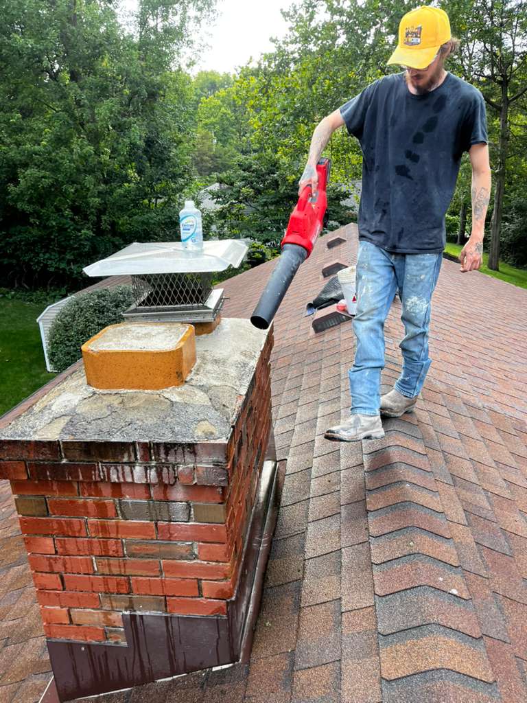Technician clearing a worn chimney crown with a blower before resurfacing