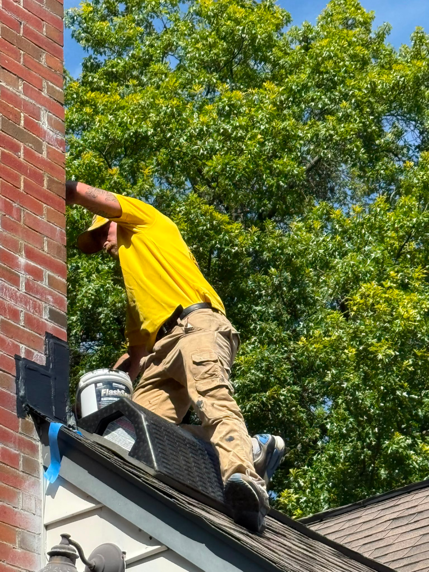 Chimney specialist working at the base of a brick chimney on a shingled roof