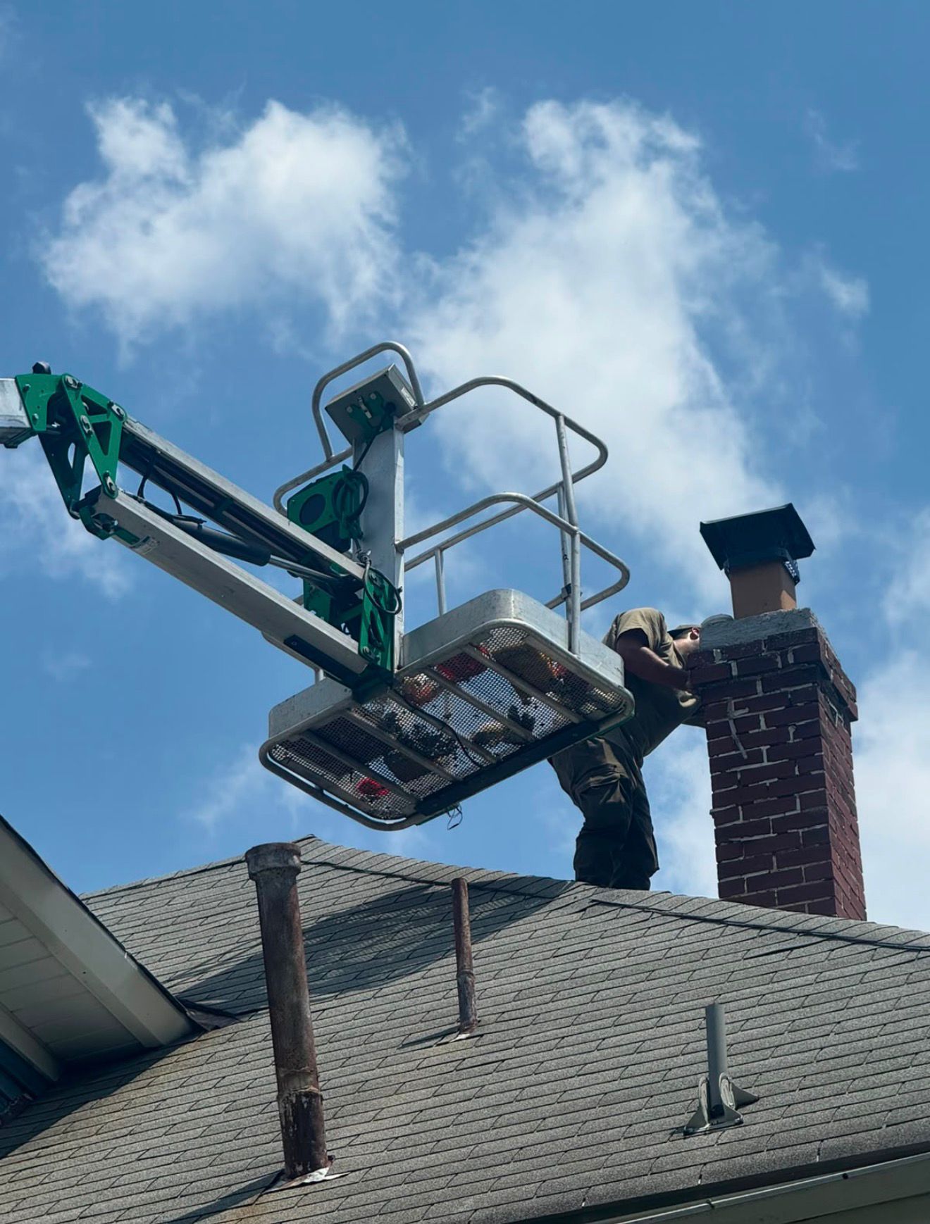 Technician working on a brick chimney from an aerial lift above the roofline